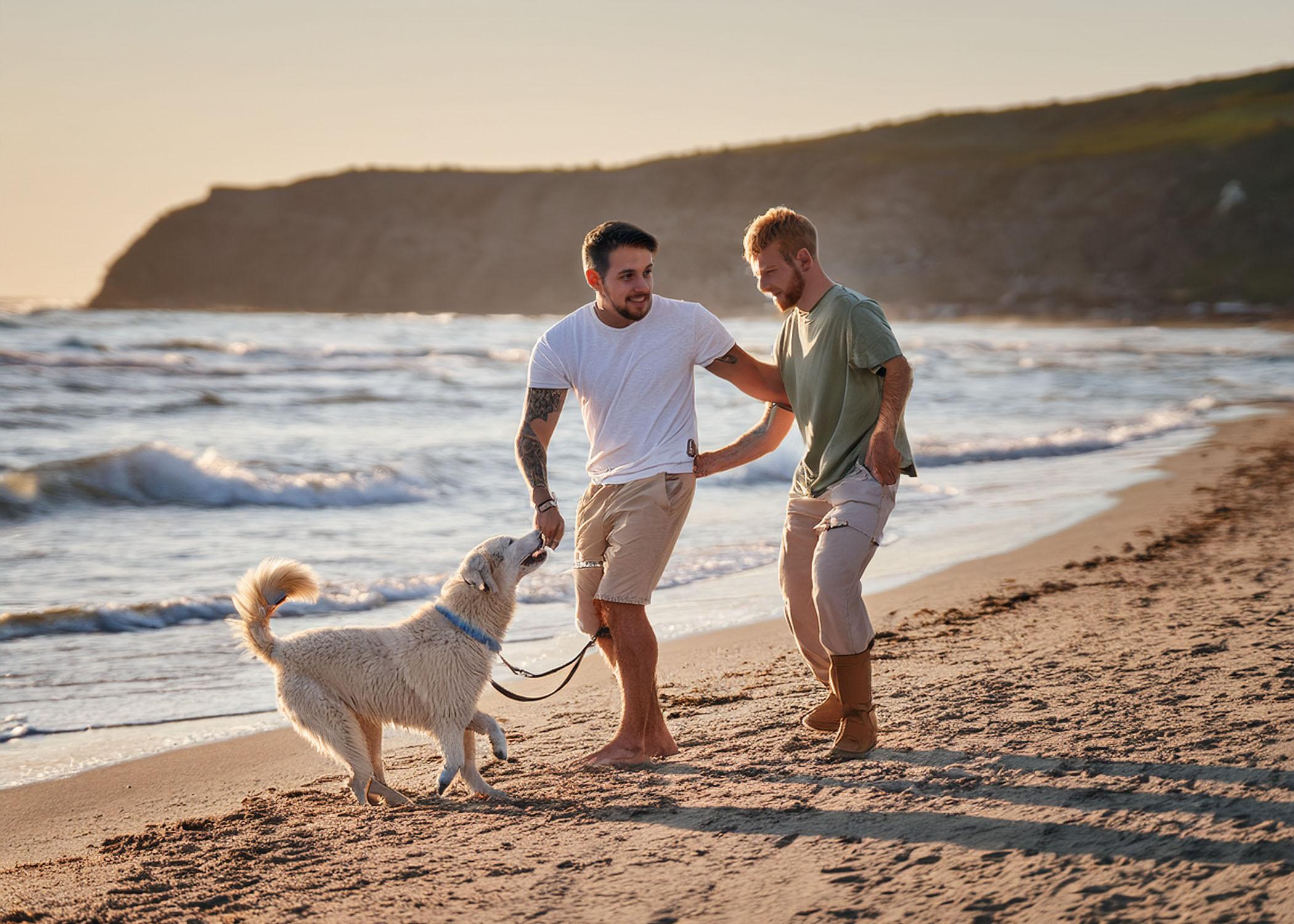 gay couple playing with dog at beach